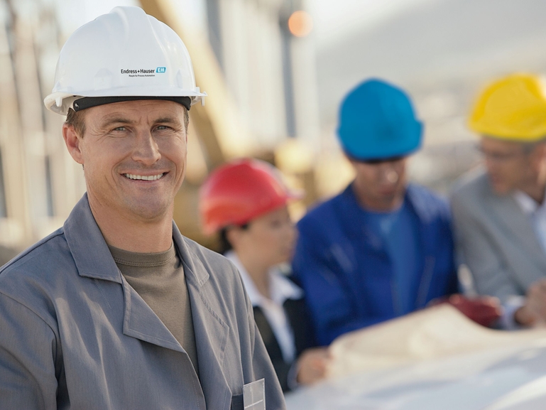 With Endress+Hauser you have a reliable partner for engineering services An Endress+Hauser engineer smiles at the camera, other engineers are behind him