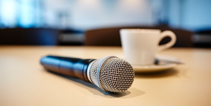 Pressekonferenzstimmung: Mikrofon und Kaffeetasse auf einem Tisch.