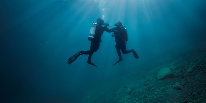 Unterwasserszene: Ein Taucher unterstützt einen zweiten Taucher mit der Luftversorgung.